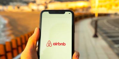 Smartphone mit Airbnb-Logo auf Strandpromenade